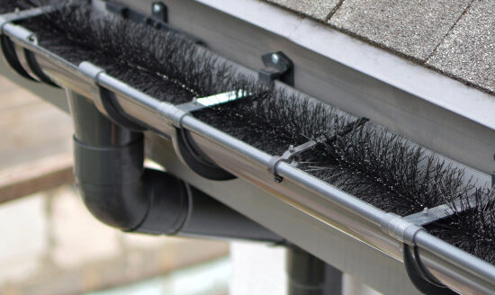 Plastic guard brush in new dark grey plastic rain gutter on asphalt shingles roof.